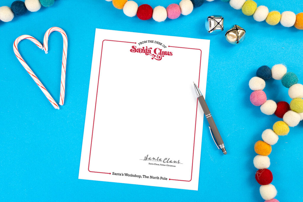 White paper with letterhead from Santa on a blue background with candy canes and felt ball garland.
