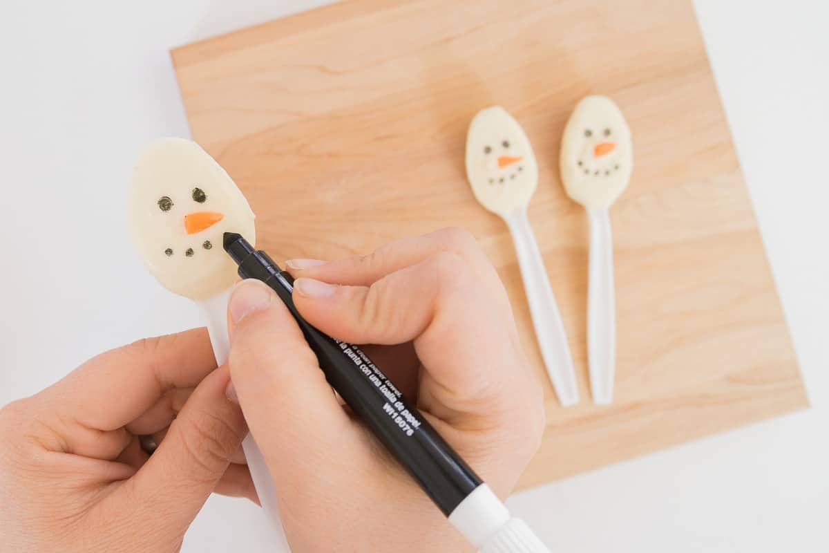 Hand using a black food-safe marker to make snowman face.