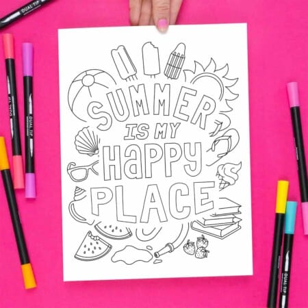 Hand holding the Summer Happy Place Coloring page on a bright pink background, surrounded by markers.